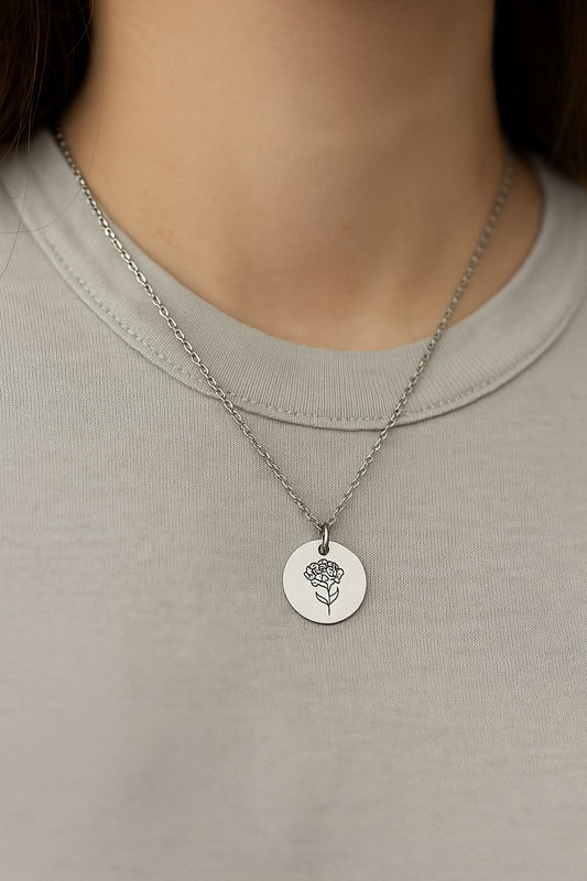 Silver necklace with a round pendant featuring a floral design on a plain shirt.