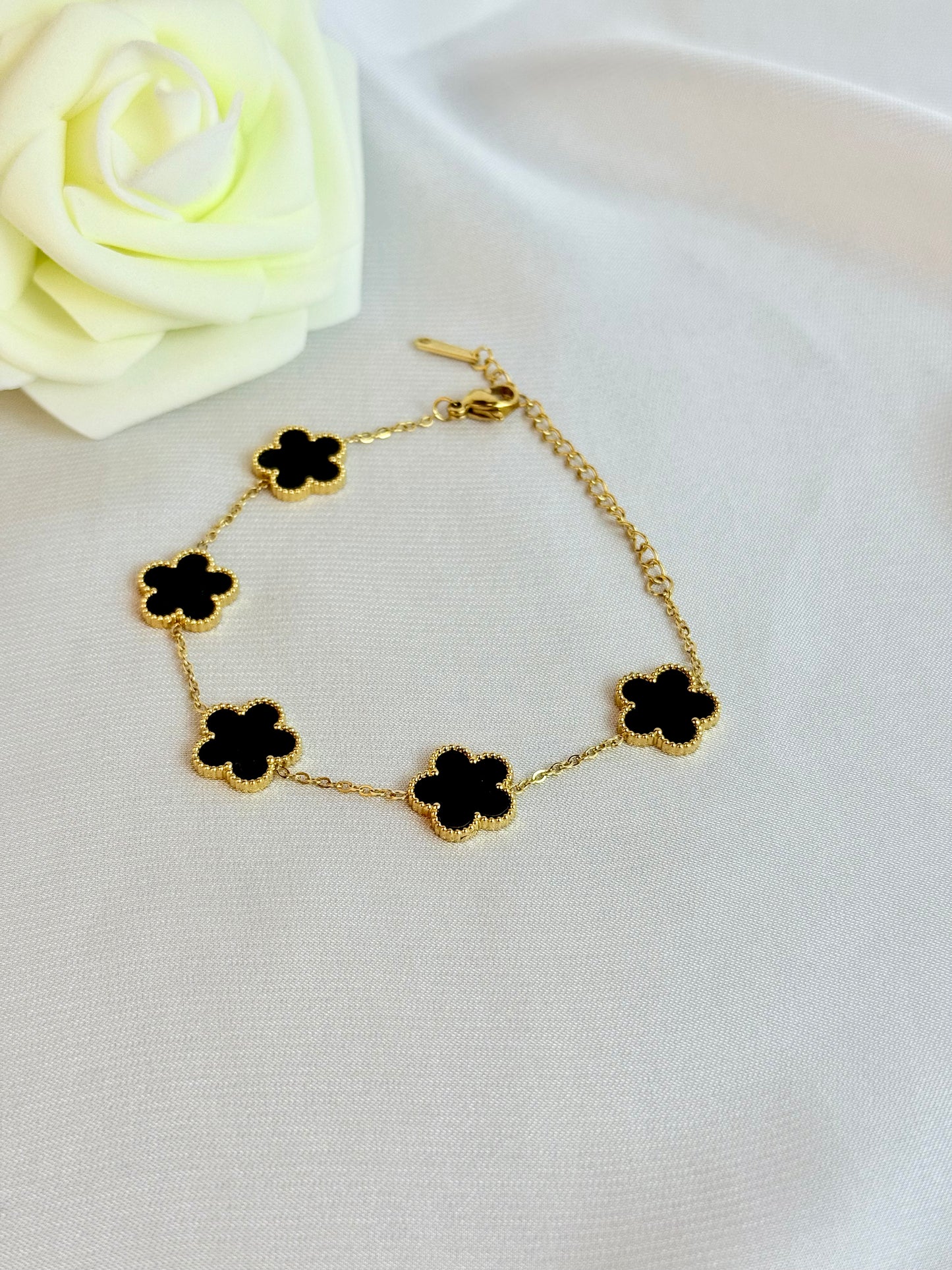 Gold bracelet with black clover-shaped charms on a white surface with a white rose.