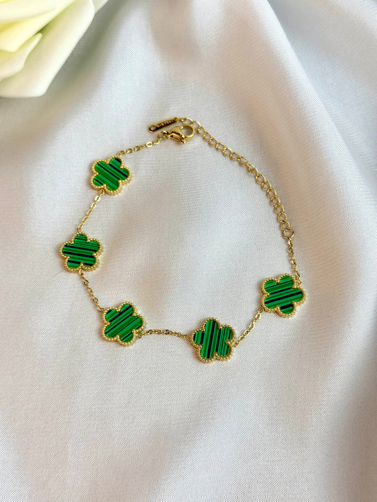 Gold bracelet with green clover-shaped charms on a white fabric background