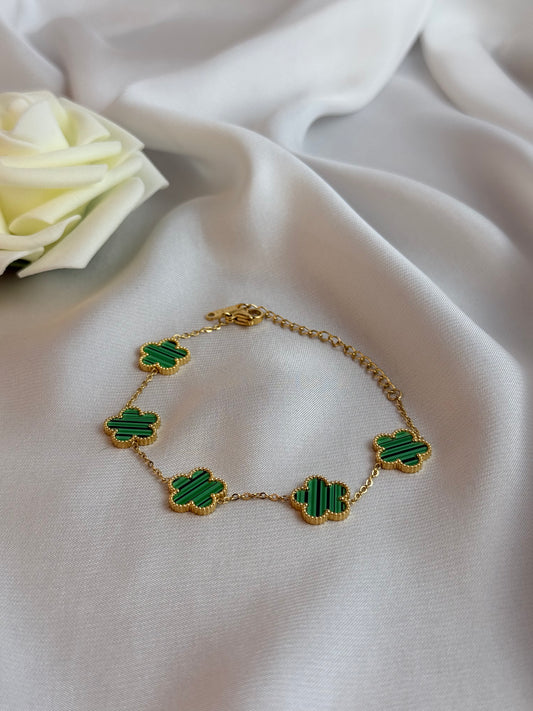 Gold bracelet with green clover-shaped charms on a white fabric background