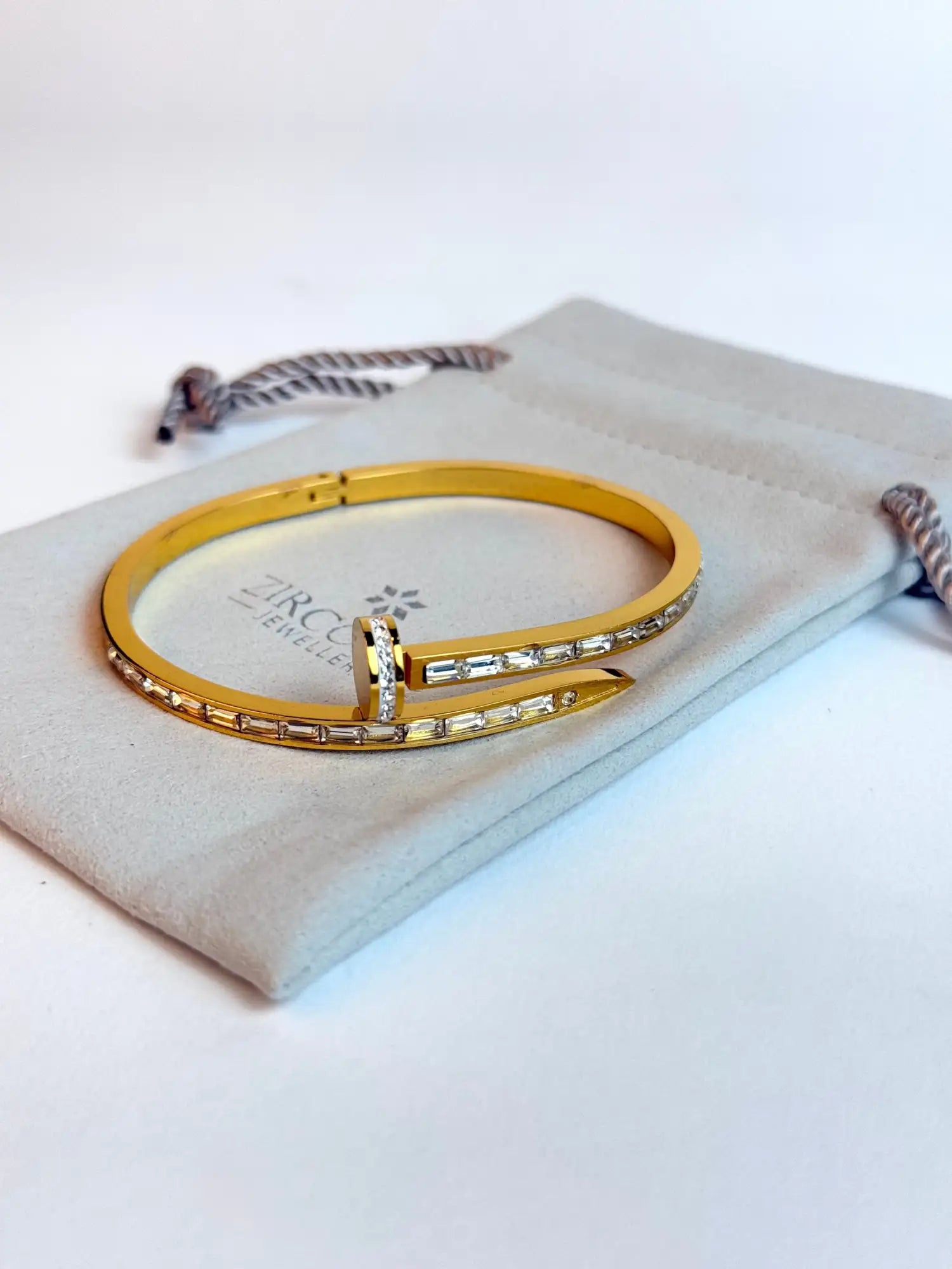 Gold-toned bangle bracelet with a sleek, modern design featuring embedded baguette-cut clear stones and a central clasp adorned with smaller diamonds.
