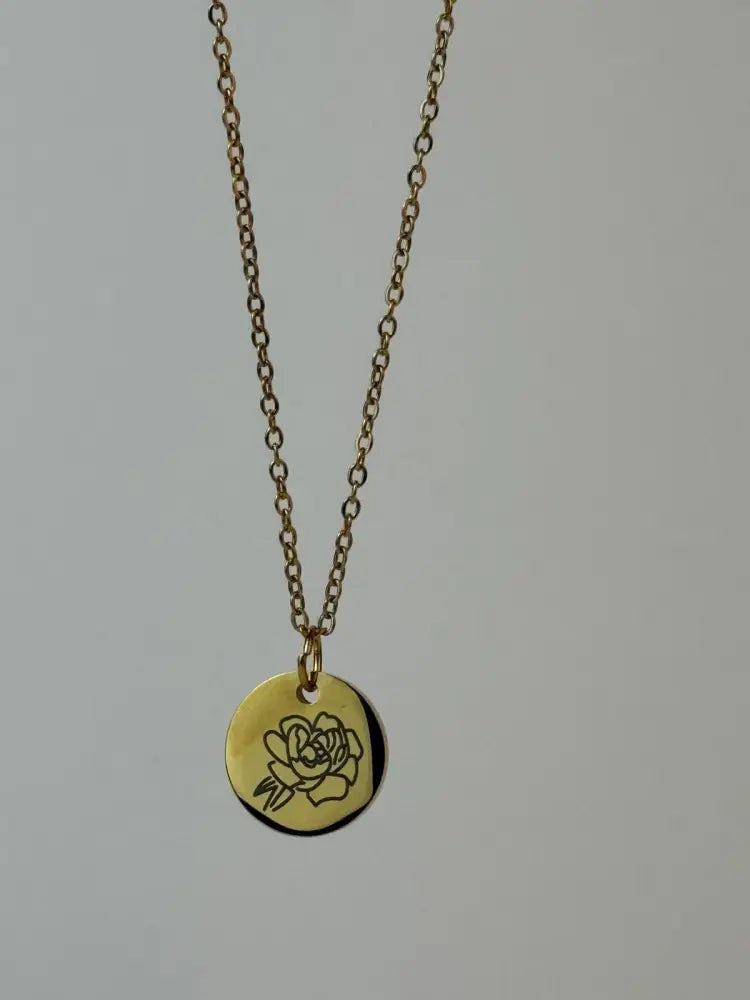 Gold necklace with a round pendant featuring a rose design on a gray background