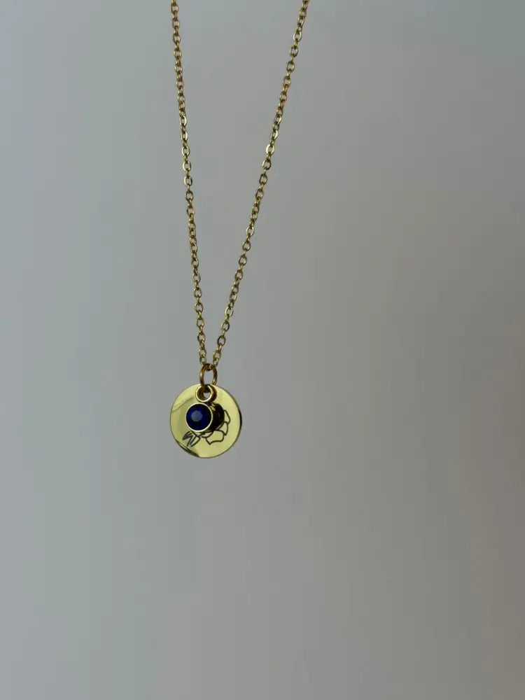 Gold necklace with a round pendant featuring a blue gemstone on a gray background