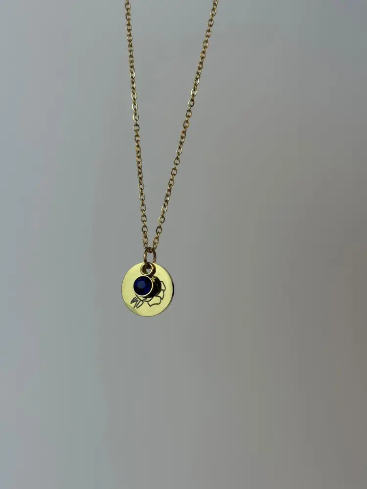 Gold necklace with a round pendant featuring a blue gemstone on a gray background