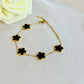 Gold bracelet with black clover-shaped charms on a white surface with a white rose.