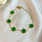 Gold bracelet with green clover-shaped charms on a white fabric background