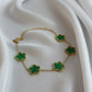 Gold necklace with green clover-shaped pendants on a white fabric background