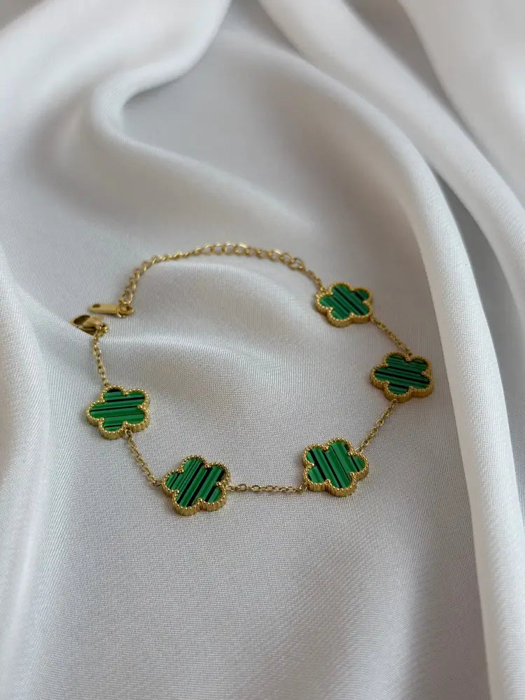 Gold necklace with green clover-shaped pendants on a white fabric background