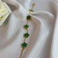 Gold bracelet with green clover-shaped charms on a white fabric background
