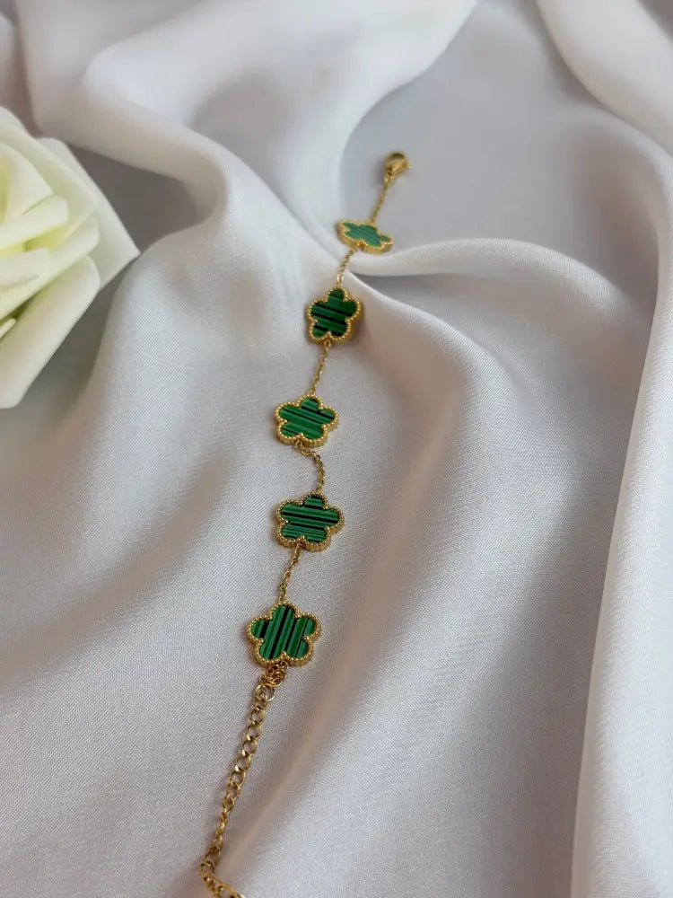 Gold bracelet with green clover-shaped charms on a white fabric background