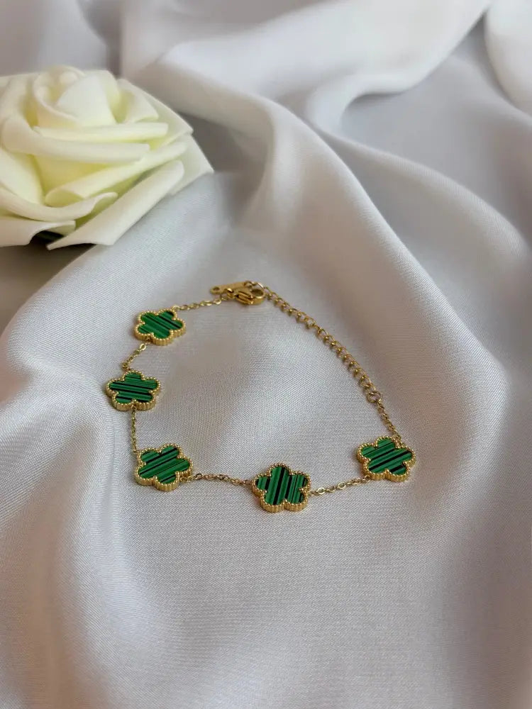 Gold bracelet with green clover-shaped charms on a white fabric background