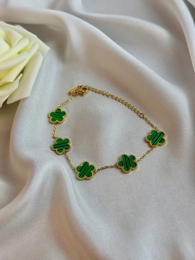 Gold bracelet with green clover-shaped charms on a white fabric background