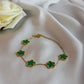Gold bracelet with green clover-shaped charms on a white fabric background