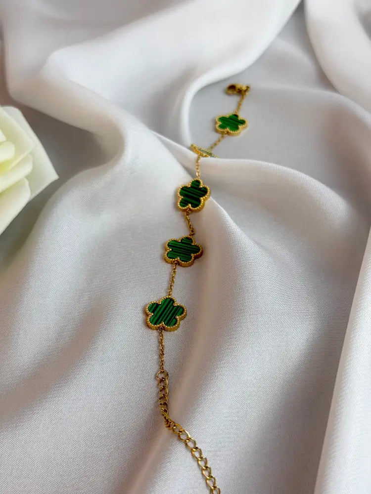 Gold bracelet with green clover charms on a white fabric background
