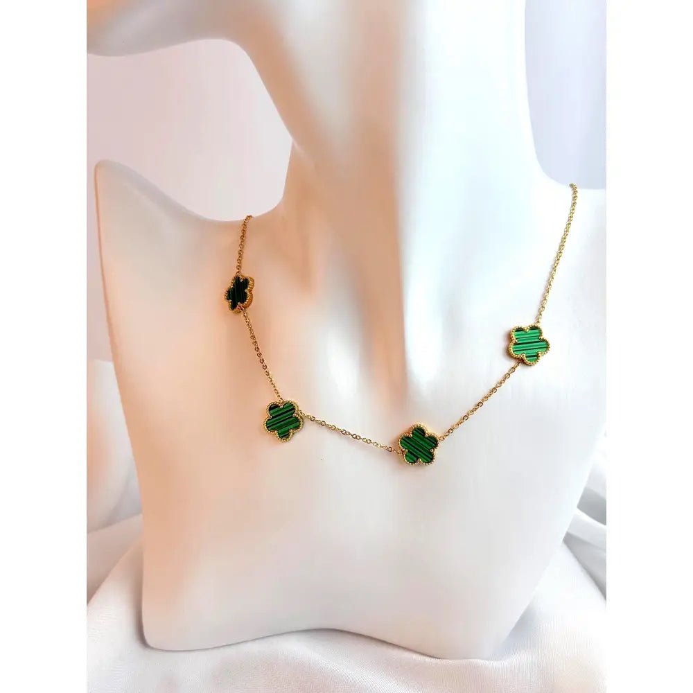 Gold necklace with green clover-shaped pendants on a white cushion