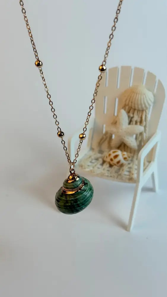 Necklace with a green pendant on a white surface, with a small chair and shells in the background.