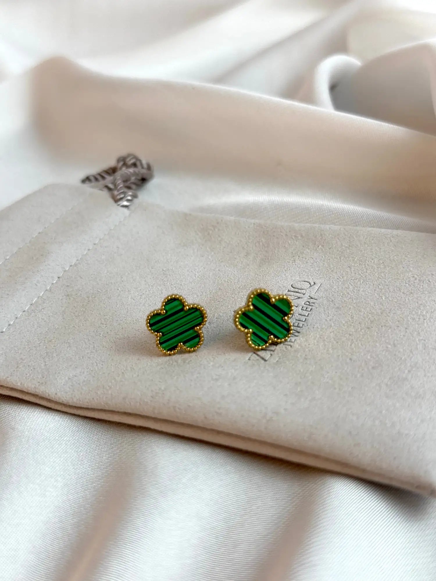 Green four-leaf clover-shaped earrings with gold-tone edges, featuring a striped pattern and set in a velvet pouch.