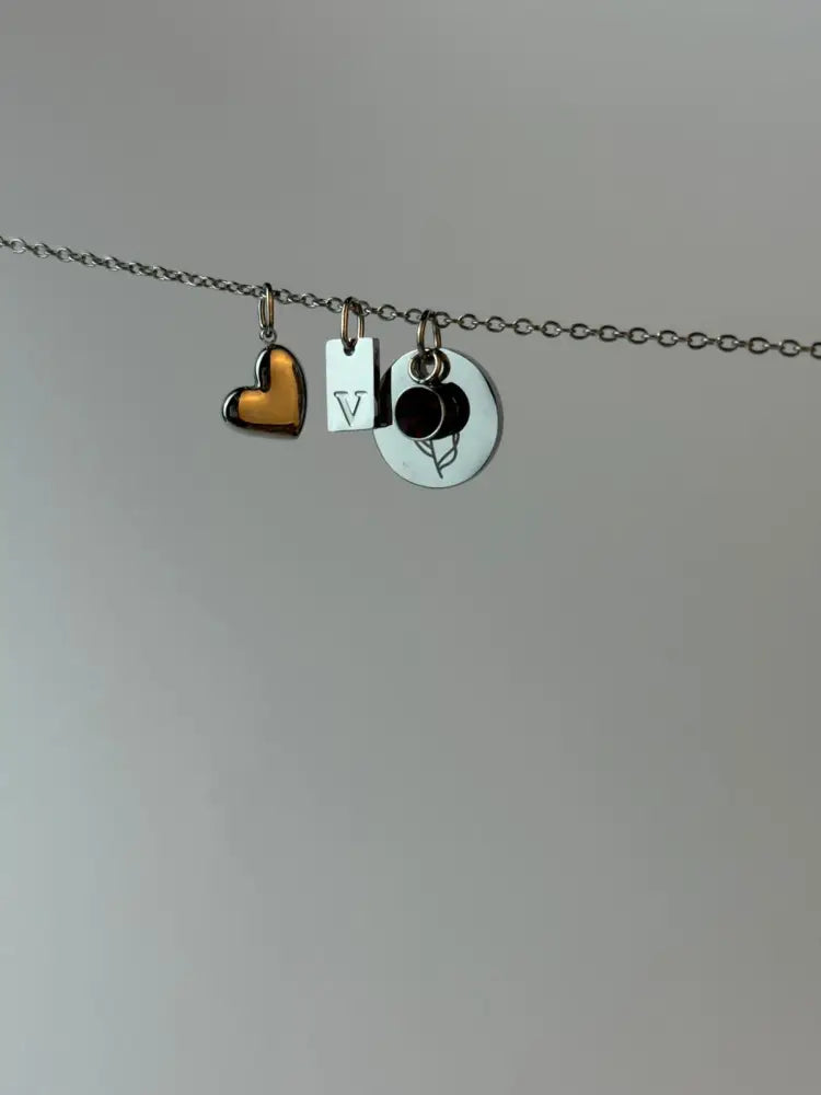 Necklace with heart, letter 'V', and circular charm on a plain background