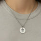 Silver necklace with a round pendant featuring a floral design on a plain shirt.