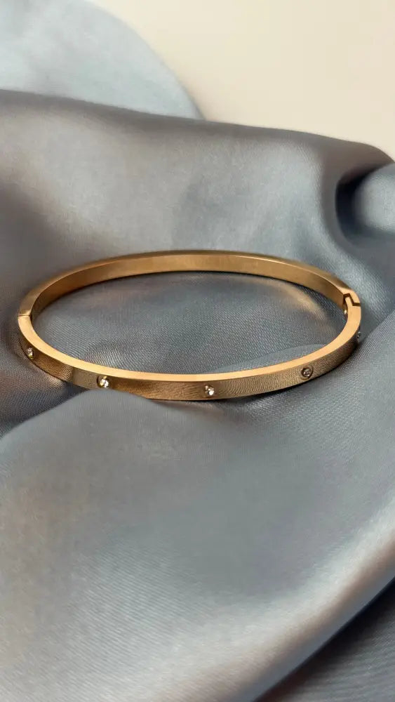 Gold bracelet on a gray fabric surface
